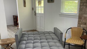 A room with a large grey sofa, a patterned rug, a wicker chair, and a door with a window. - Spacious and marvelous studio with AC in quiet urban setting (Raleigh)