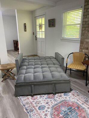 Ein Zimmer mit einem großen grauen Sofa, einem gemusterten Teppich, einem Korbstuhl und einer Tür mit einem Fenster.