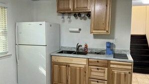 A kitchen with wooden cabinets, a white refrigerator, a sink with a faucet, and a countertop with a dish soap bottle. - Spacious and marvelous studio with AC in quiet urban setting (Raleigh)