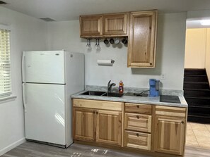 Eine Küche mit Holzschränken, einem weißen Kühlschrank, einer Spüle mit Armatur und einer Arbeitsplatte mit einer Flasche Geschirrspülmittel.