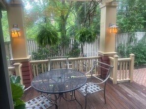 A covered outdoor patio with a round metal table and chairs, surrounded by a wooden deck and a white picket fence.
