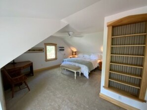 A bedroom with a bed, a desk, a chair, a window, and a built-in shelf.