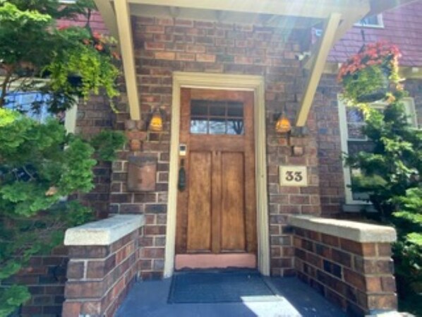A brick building with a wooden door, a number '33' sign, and two wall-mounted lights.