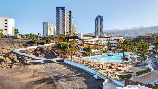 Un resort con piscina, palmeras y rascacielos al fondo.