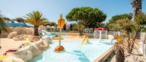 A swimming pool with a rock-lined edge, a water slide, and a palm tree.