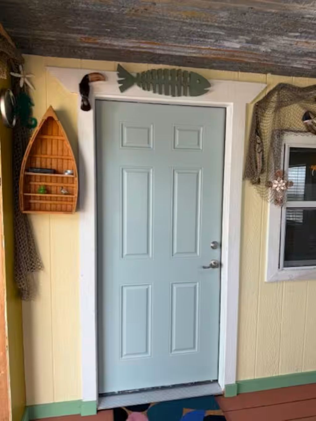 A door with a decorative fish hanging above it, a small wooden boat on the wall, and a window with a decorative wreath.