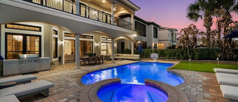 Una casa de dos pisos con piscina, mobiliario exterior y un patio.