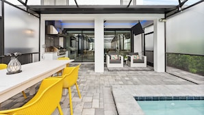 A modern outdoor patio with a dining area, yellow chairs, a pool, and a view into the house. - Theater | Themed Kids Bedrooms | Games Room | Private Pool (Kissimmee)