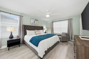 Ein Schlafzimmer mit Bett, Nachttisch, Lampe, Sessel, Schreibtisch und Deckenventilator.