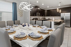 A modern kitchen with dark cabinets, stainless steel appliances, and a dining area set for a meal. - Luxury Home with Kids Themed Bedrooms, Games Room and Private Pool! (Davenport)