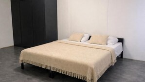 Un dormitorio con una cama, un armario oscuro y una pared lisa.