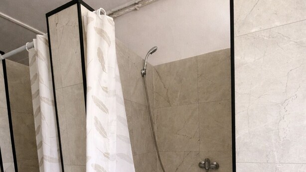 Una zona de ducha con puerta de cristal, cabezal de ducha y cortina.