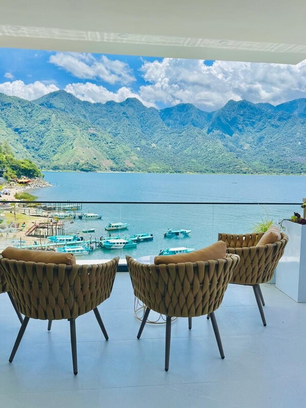 Une terrasse avec des chaises en osier et une vue sur un lac où naviguent des bateaux.