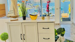 A room with a large window, a cabinet with drawers, a potted plant, and a small table with a decorative item. - Luxury Atitlan Apartamentos  (San Pedro La Laguna)