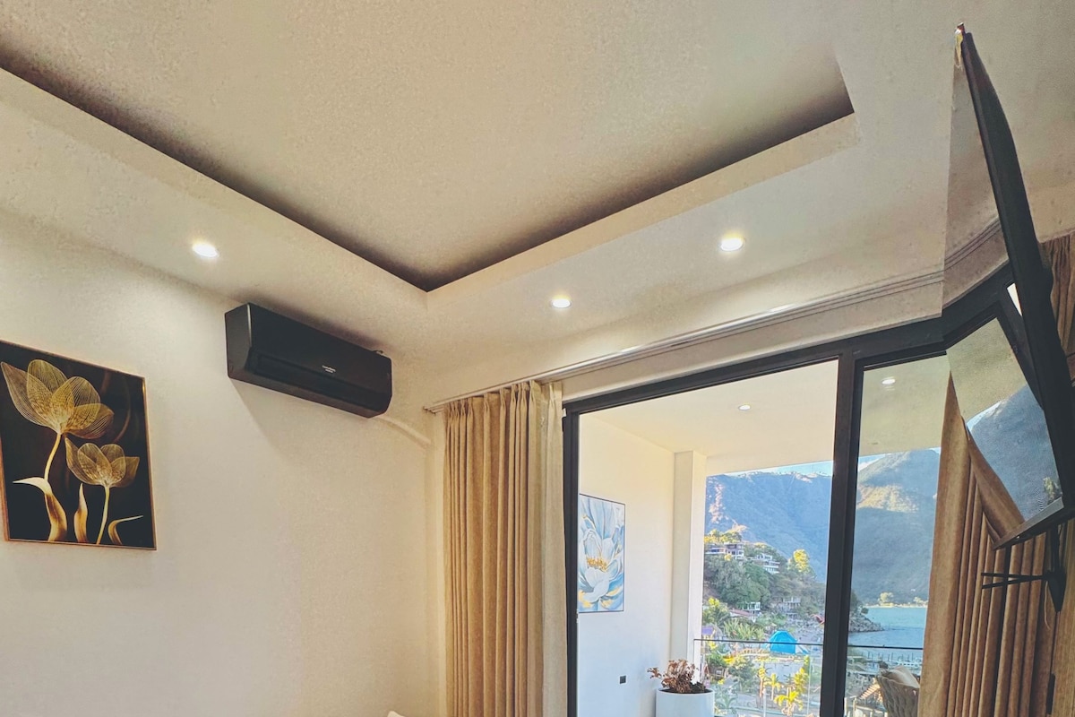 Een moderne woonkamer met een gebogen bank, een flatscreen televisie aan de wand en een grote schuifpui die leidt naar een buitenbalkon.