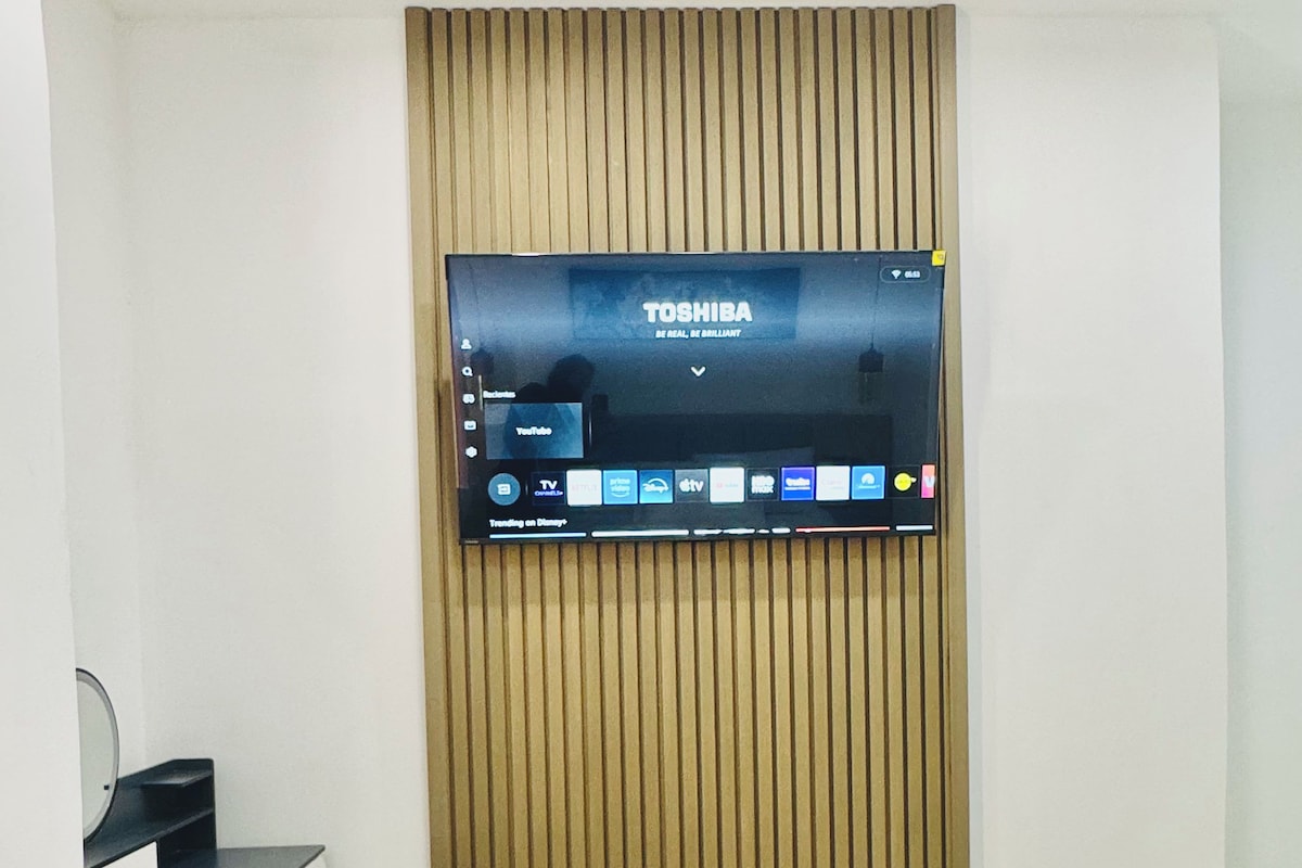 Een hotelkamer met een bed, een bureau met stoel en een tv met een startscherm.