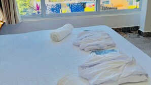 A hotel room with a bed, a window with a view of a lake and mountains, and a neatly made bed with towels. - Luxury Atitlan Apartamentos  (San Pedro La Laguna)
