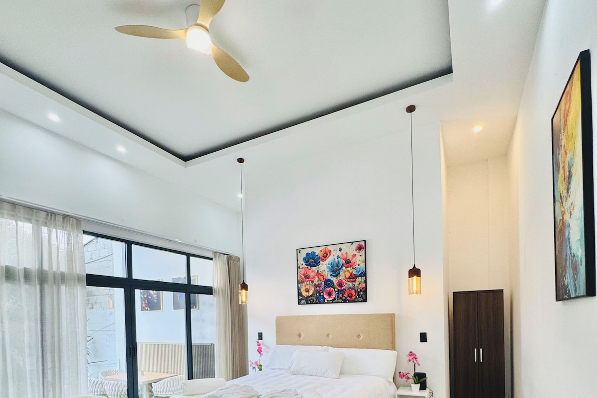 Een moderne slaapkamer met een groot bed, een plafondventilator, een schilderij en uitzicht op de omgeving.