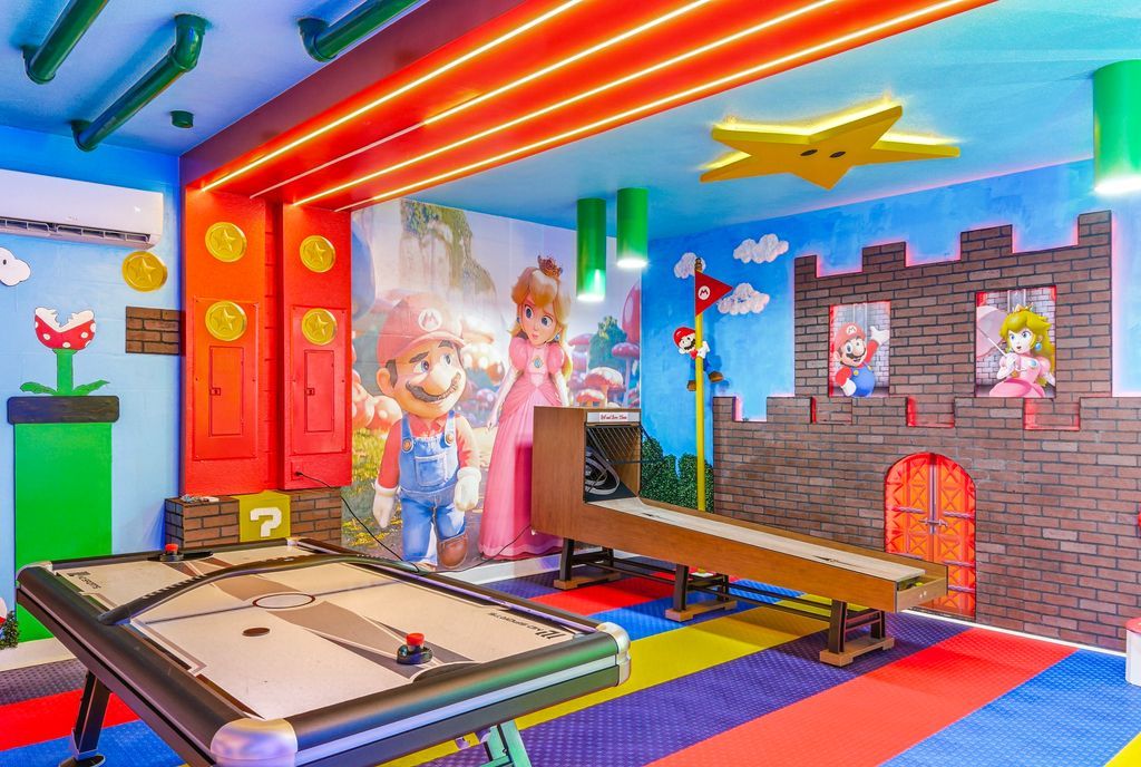 Una habitación colorida con una mesa de fútbol de mesa, carteles de Mario y la Princesa Peach, y un diseño de pared de ladrillo.