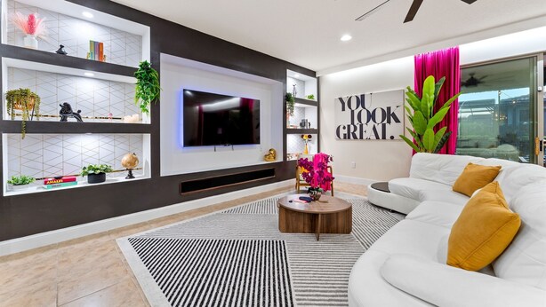 Ein modernes Wohnzimmer mit Flachbildfernseher, Deckenventilator, einem weißen Sofa und einem Bücherregal mit Dekoration.