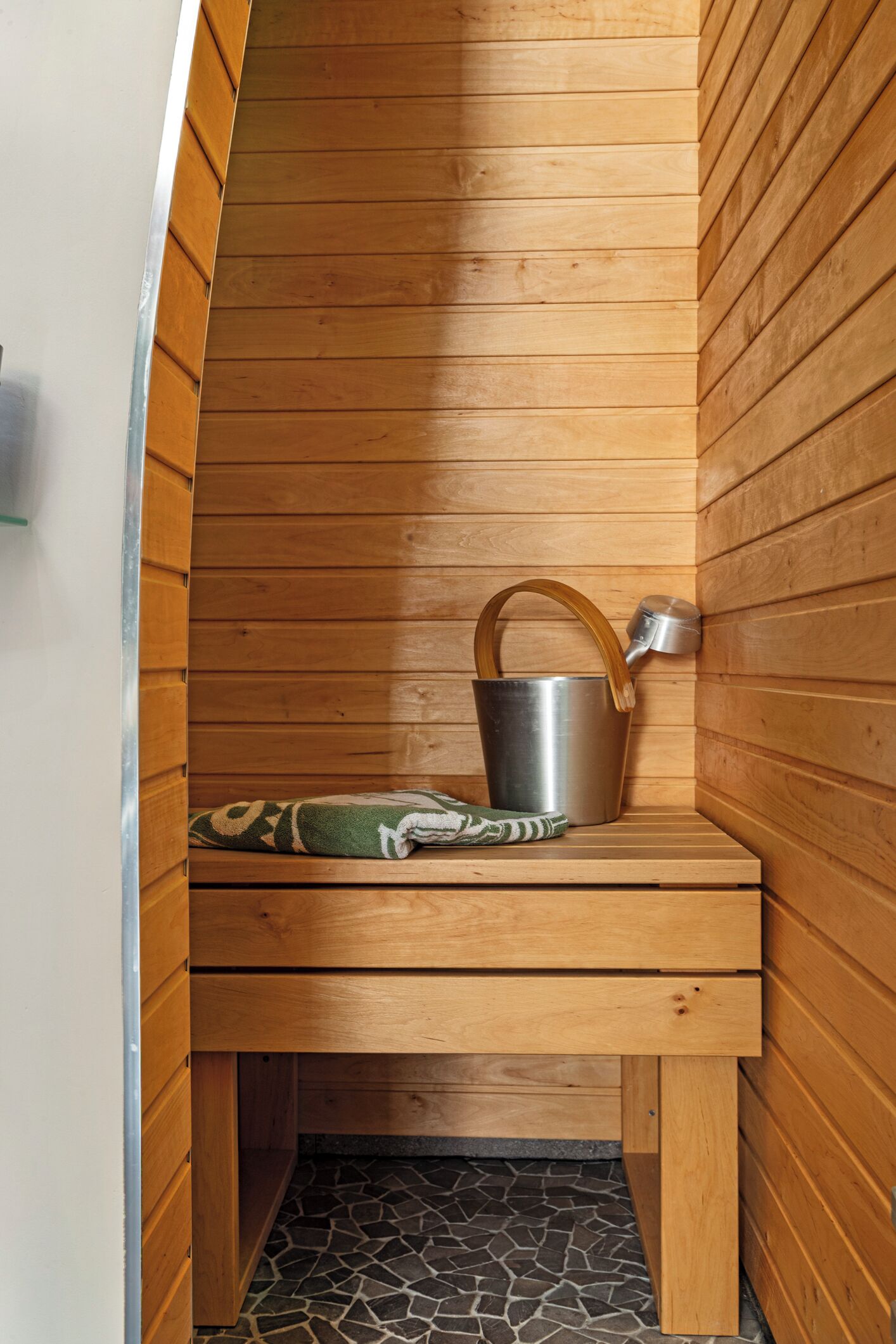 Un sauna avec des murs en bois, un banc, un seau en métal et une serviette.