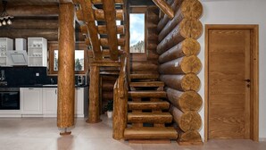 Interior de una cabaña de troncos con una escalera en espiral, paredes de madera, una zona de cocina y una puerta.