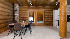 Interior de una cabaña de troncos con comedor, cocina y un jacuzzi tipo spa.