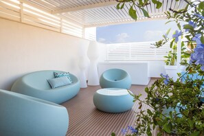 A modern outdoor seating area with round, light-colored sofas and a white planter with blue flowers. - Dimora Zahira, Design Suites 2 min from the Sea - New - Center (Marina di Ragusa)