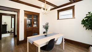 Spiseområde med bord, stole, lysekrone, skab og et vindue.