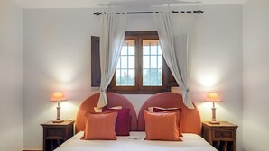 Un dormitorio con una cama, dos mesitas de noche, dos lámparas, un ventanal con cortinas y un cabecero.