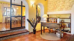 Un vestíbulo de hotel con zona de comedor, pared de piedra, lámpara y un florero con plantas.