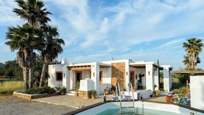 Un edificio blanco con piscina, rodeado de palmeras y plantas.