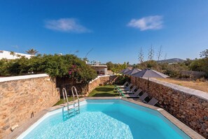 A swimming pool with a stone wall, a grassy area, and lounge chairs.
