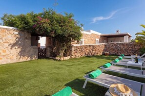 A courtyard with a stone wall, a grassy lawn, and white lounge chairs with green towels.