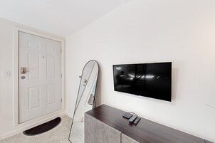 Una habitación con una puerta blanca, un televisor de pantalla plana montado en la pared y un mueble de madera oscura con un control remoto encima.