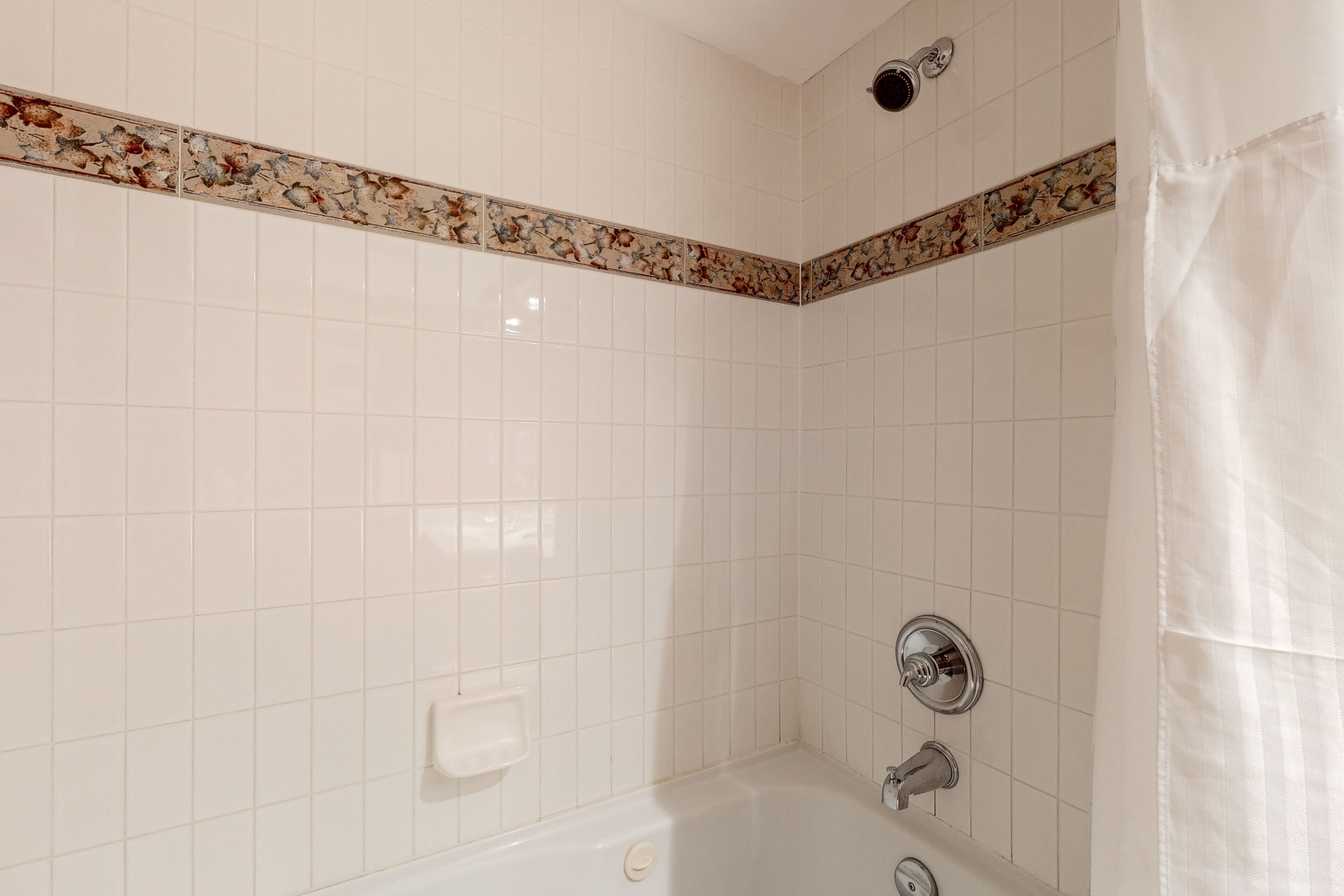Une petite salle de bain avec des murs recouverts de carreaux blancs, une baignoire et une douche.
