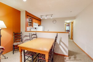 A dining area with a wooden table and chairs, a microwave, and a clock on the wall.