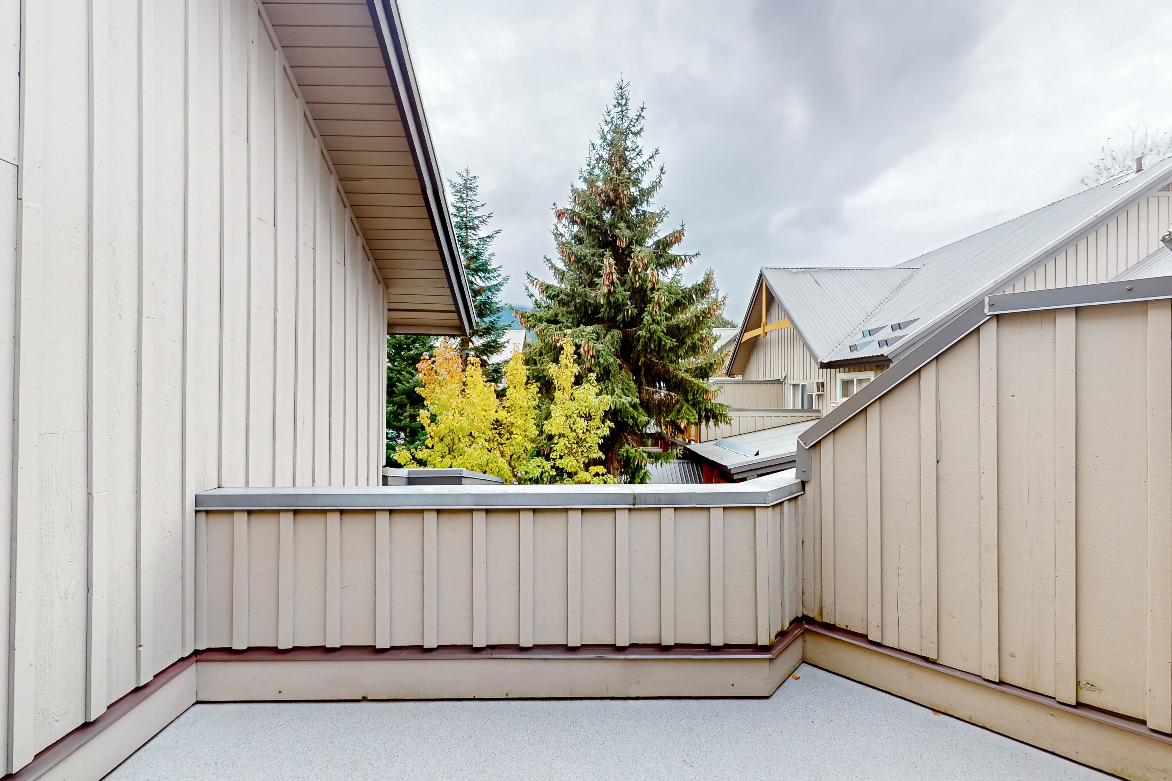 A narrow balcony with a view of a coniferous tree and neighboring buildings.