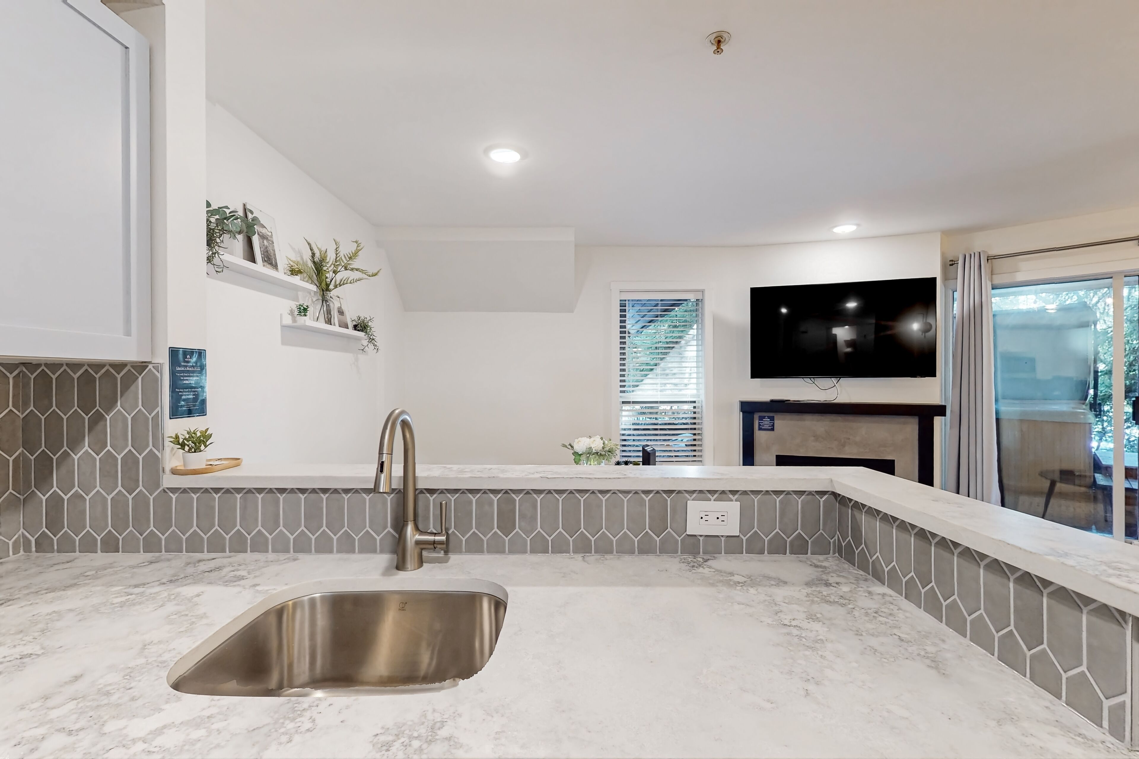 Una cocina moderna con un lavamanos de acero inoxidable, un salpicadero gris con diseño y un televisor de pantalla plana montado sobre la encimera.