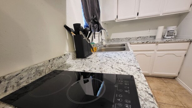 A kitchen with a black induction cooktop, white cabinets, and a granite countertop.