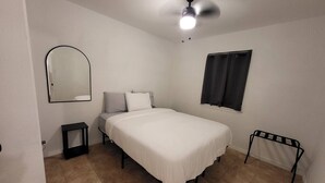 A bedroom with a bed, a ceiling fan, a window, and a mirror.