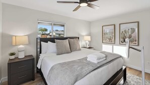 Un dormitorio con cama, mesitas de noche, ventilador de techo y obras de arte en las paredes.