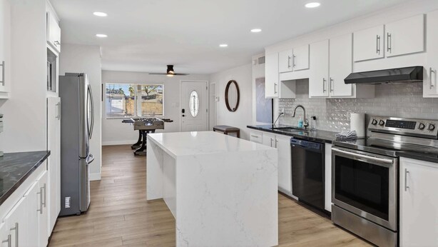 Una cocina moderna con armarios blancos, una isla de mármol, electrodomésticos de acero inoxidable y una viga de techo de madera.