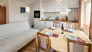 A compact kitchen with white cabinets, a dining table set for four, and a sofa in the living area. - Stunning apartment in Omisalj with WiFi (Omisalj)