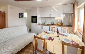 A compact kitchen with white cabinets, a dining table set for four, and a sofa in the living area. - Stunning apartment in Omisalj with WiFi (Omisalj)