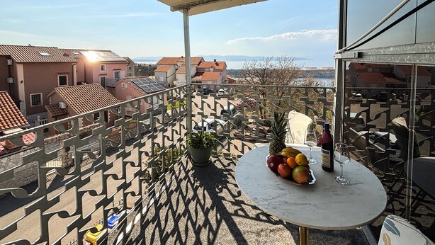 A balcony with a table, potted plants, and a view of buildings and water. - Stunning apartment in Omisalj with WiFi (Omisalj)