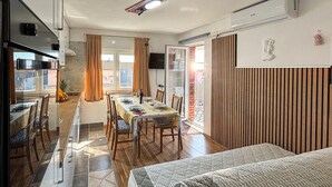 A dining area with a table set for four, a kitchen with a stove, and a sliding glass door to a balcony. - Stunning apartment in Omisalj with WiFi (Omisalj)