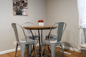 Un coin repas comprenant une table ronde et quatre chaises en métal, un vase avec des fleurs et une œuvre d’art accrochée au mur.