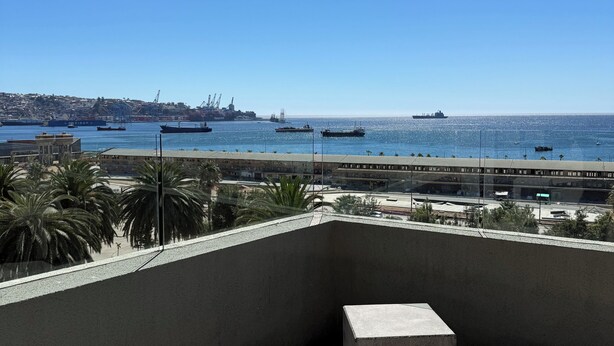 A balcony with two concrete stools, a clear view of the sea, and a distant cityscape. - Valpo Coast Suites · Modern Apartment + Parking + Rooftop (Valparaíso)