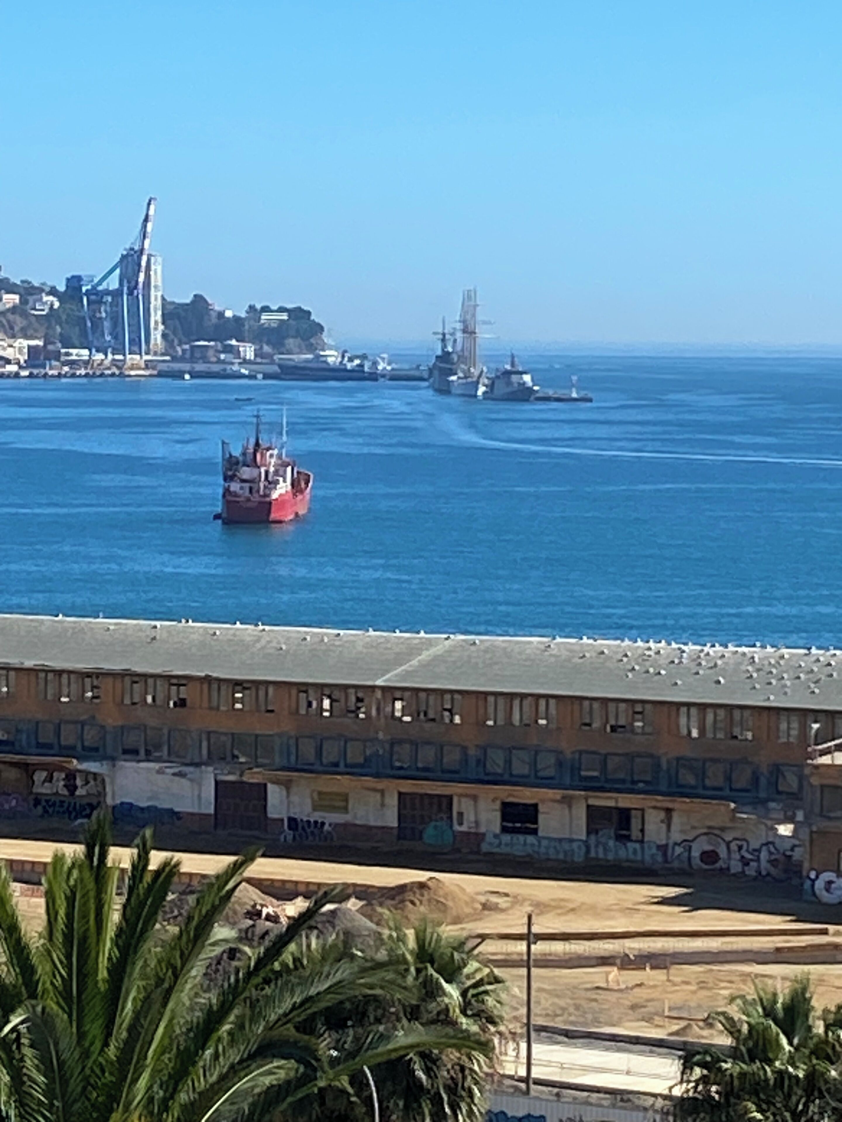 Eine Küstenansicht mit einem roten Schiff, einem großen Schiff und einem Gebäude mit Graffiti.